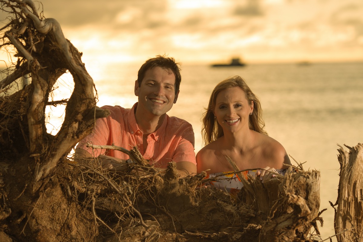young couple posing behind fallen tree, with the sea behind them 
