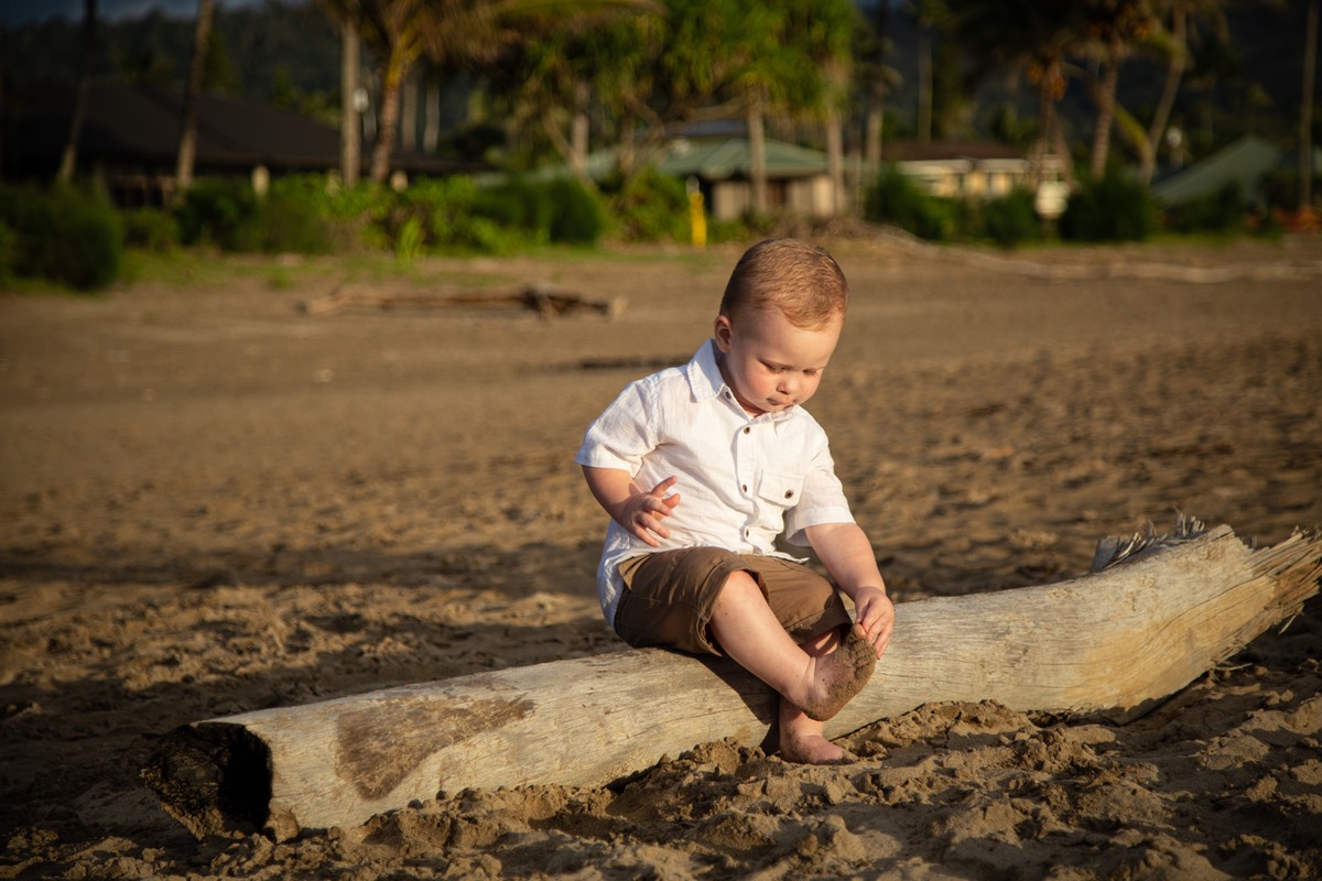Small boy sits on driftwood at the beach